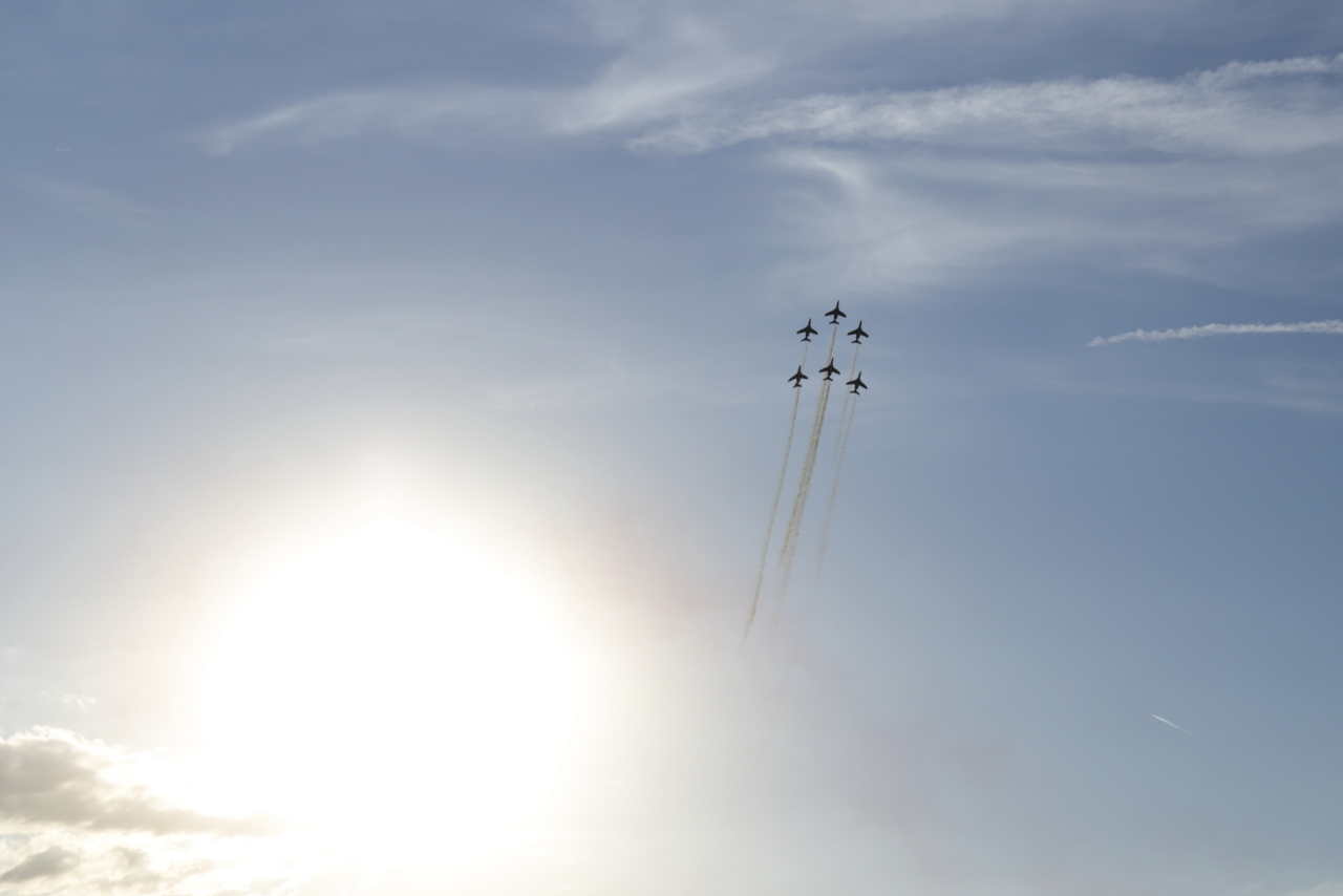 Six appareils en formation de la patrouille de France prenant de l’altitude avec des fumigènes blancs.