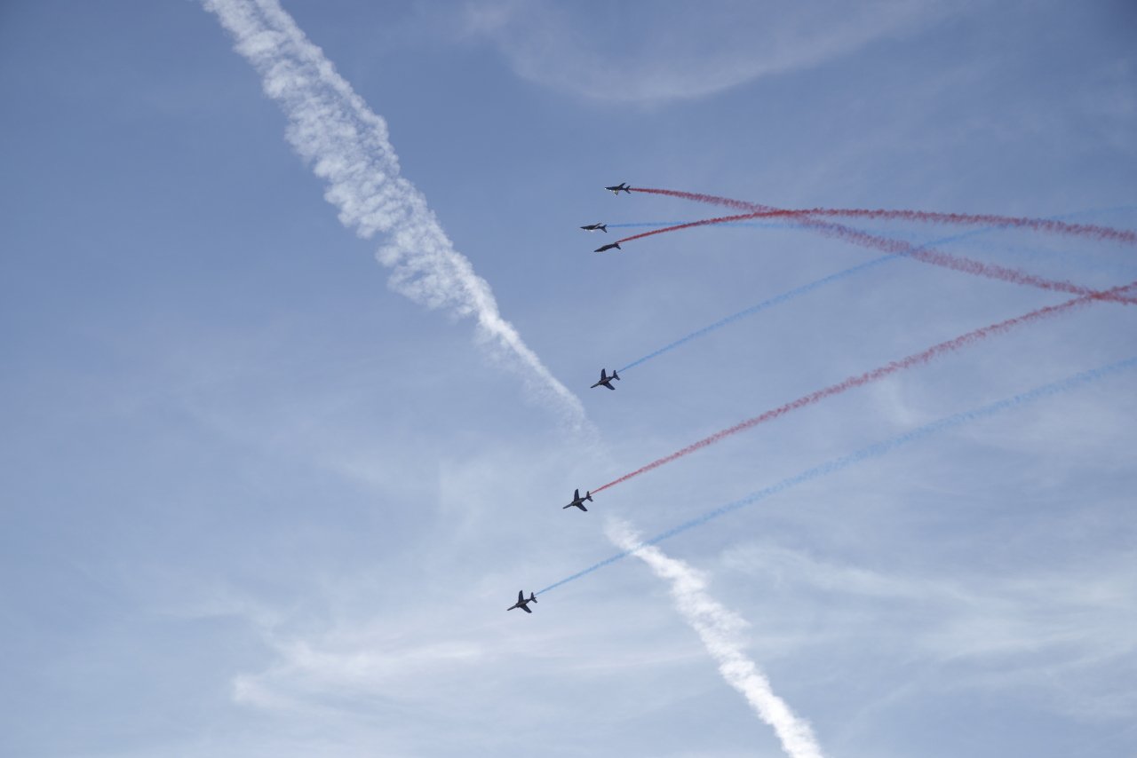 Six appareils de la patrouille de France plongeant depuis l’altitude avec des fumigènes rouges et bleus.