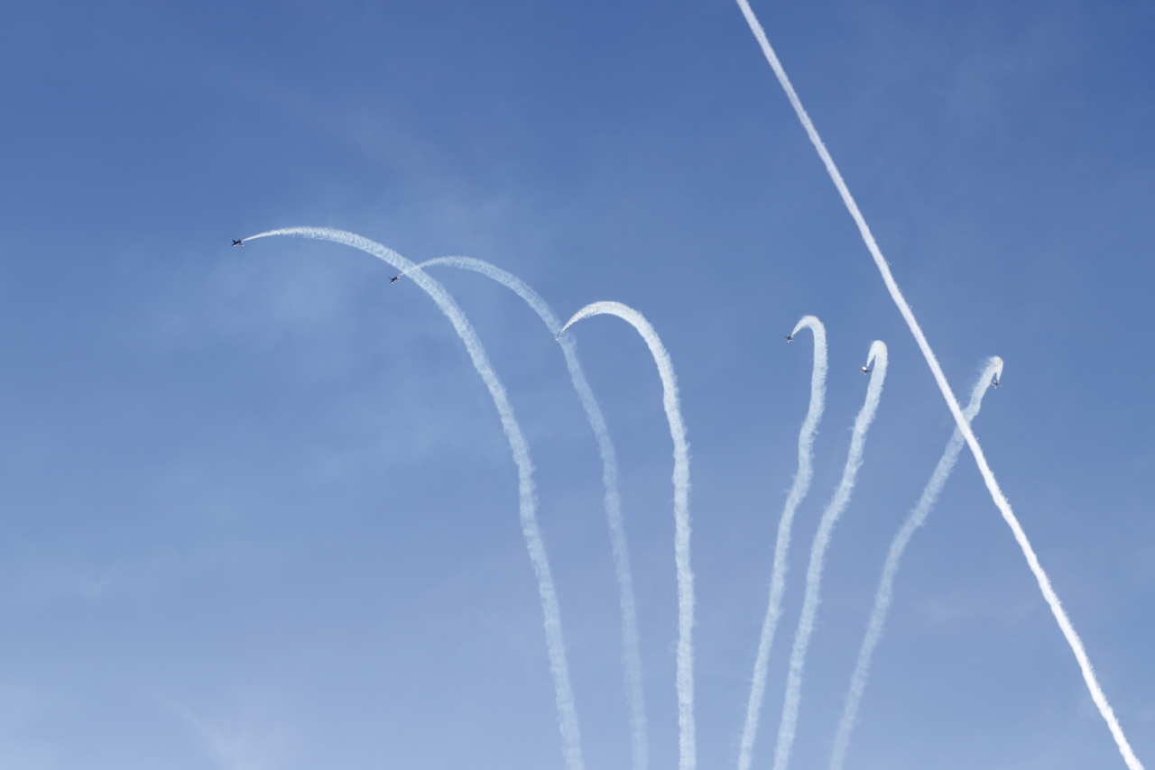 Six appareils de la patrouille de France avec des fumigènes blancs qui se retournent pour plonger avec des fumigènes blancs.