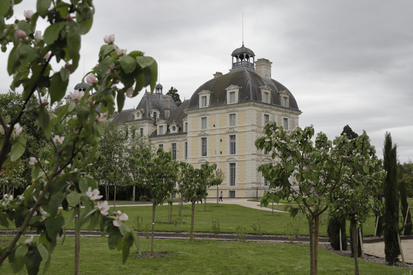 Vue sur la tour ouest du château entre des arbres depuis les jardins.